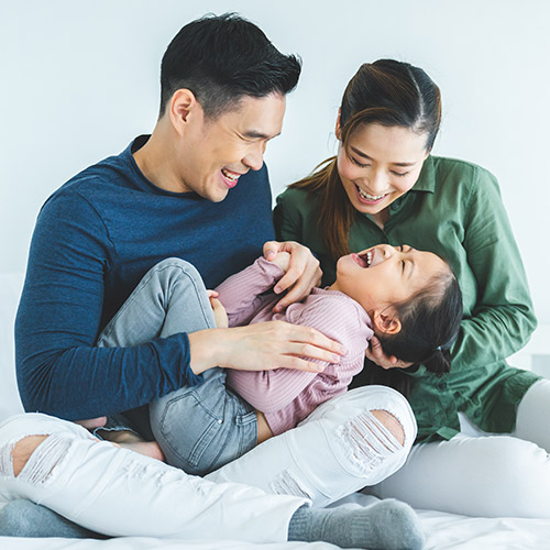 A mother, father and daughter laughing together, sitting on the floor.