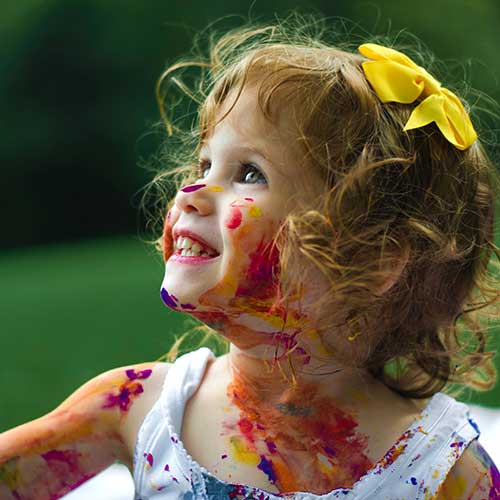 A little girl, covered in colourful paint, smiling