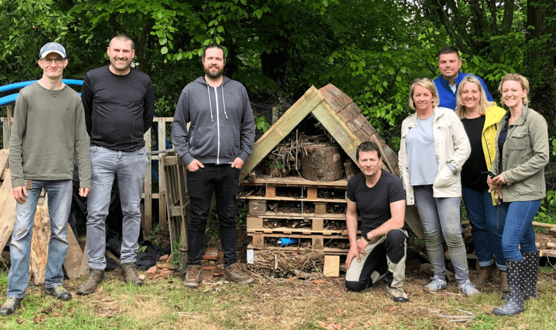 OneFamily staff posing for a picture next to a bug hotel at at Stanmer Wellbeing Gardens