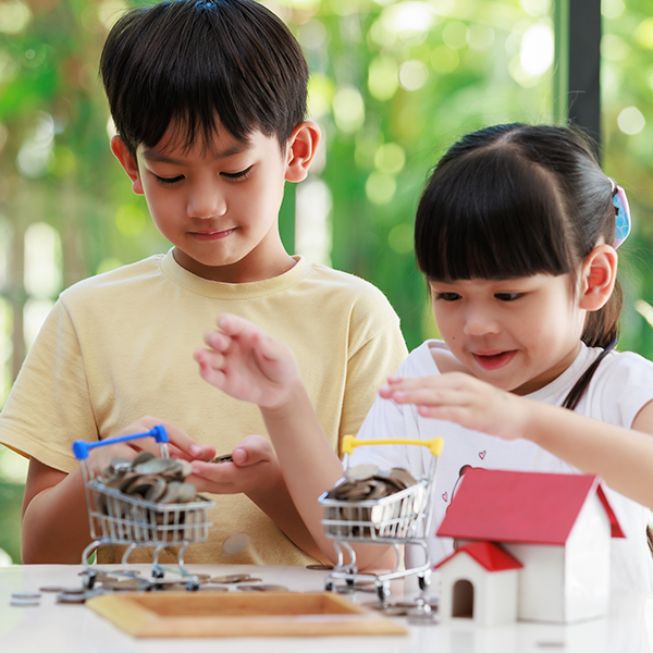 Young boy and girl putting coins in shopping cart with stack of coins and model house