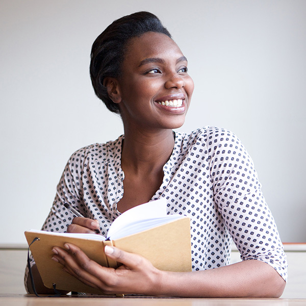 Portrait of smiling young black woman writing in journal at home