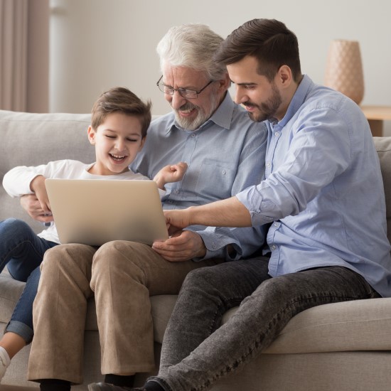 Granddad, Dad and son on a sofa looking at a laptop together