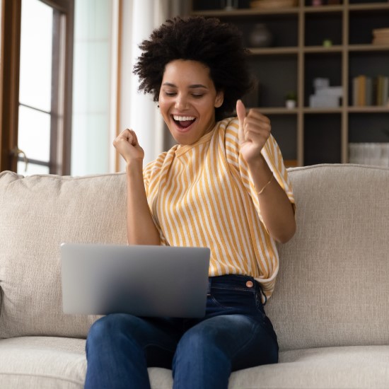 Young woman on a sofa celebrating something she's seen on a laptop