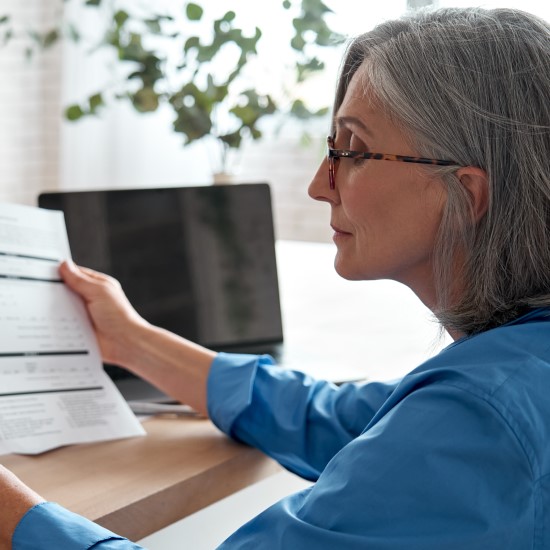 Woman looking at a bank statement next to an open laptop