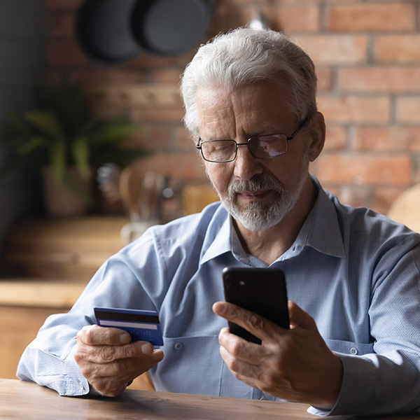 Focused mature retired man holding bank credit card, entering payment information in mobile shopping application, purchasing goods or services in online store, old people and modern tech concept.