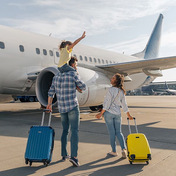 Back view of happy family standing near a large plane with two suitcases outdoor. Trip concept