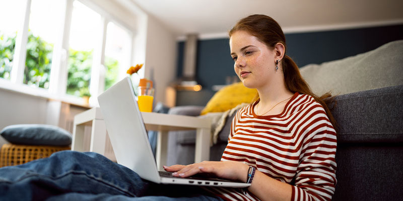 Teenage girl, using a laptop, while sitting on the floor in the living room